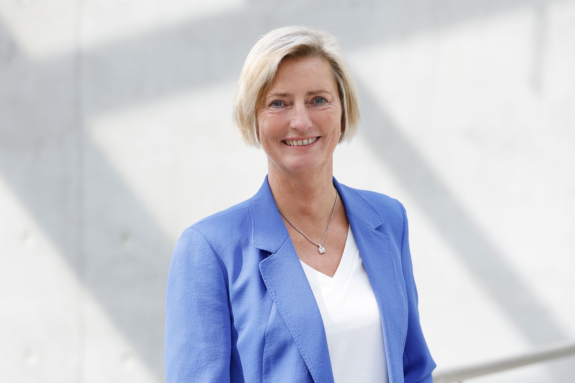 Frau in blauen Anzug vor einer Fensterfront.