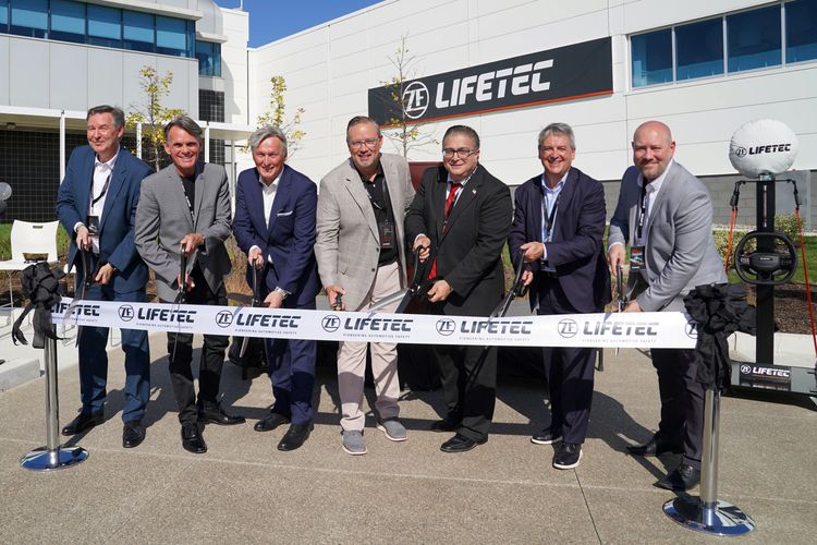 Eine Gruppe von sieben Männern in Geschäftskleidung durchschneidet während der großen Eröffnungsveranstaltung ein zeremonielles Band vor einem ZF Lifetec-Gebäude.